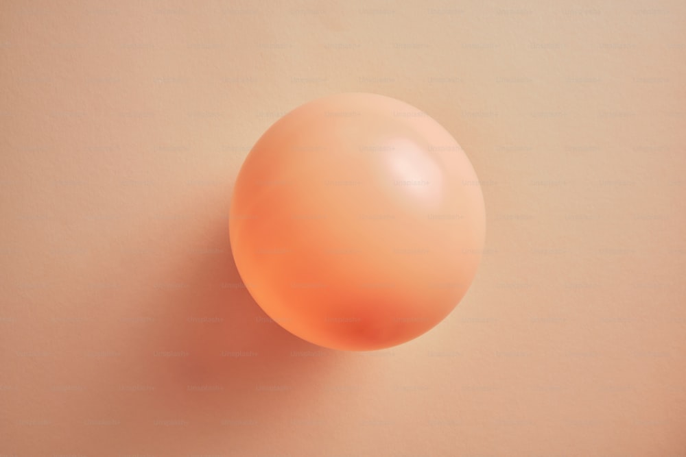una bola naranja sobre una superficie rosa claro