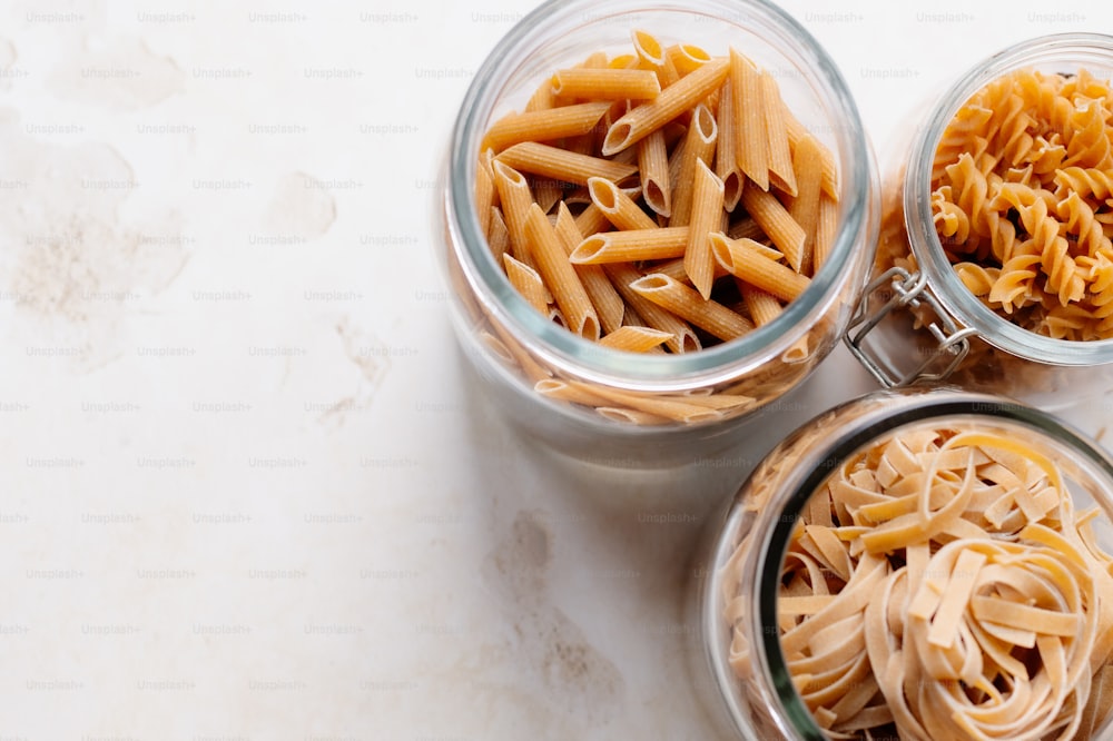three glass jars filled with different types of pasta