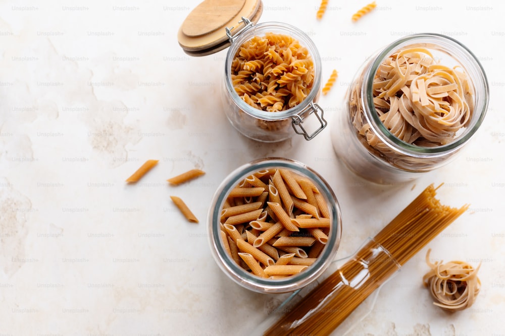 three glass jars filled with pasta noodles and a wooden spoon