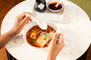 a person eating a bowl of soup with chopsticks
