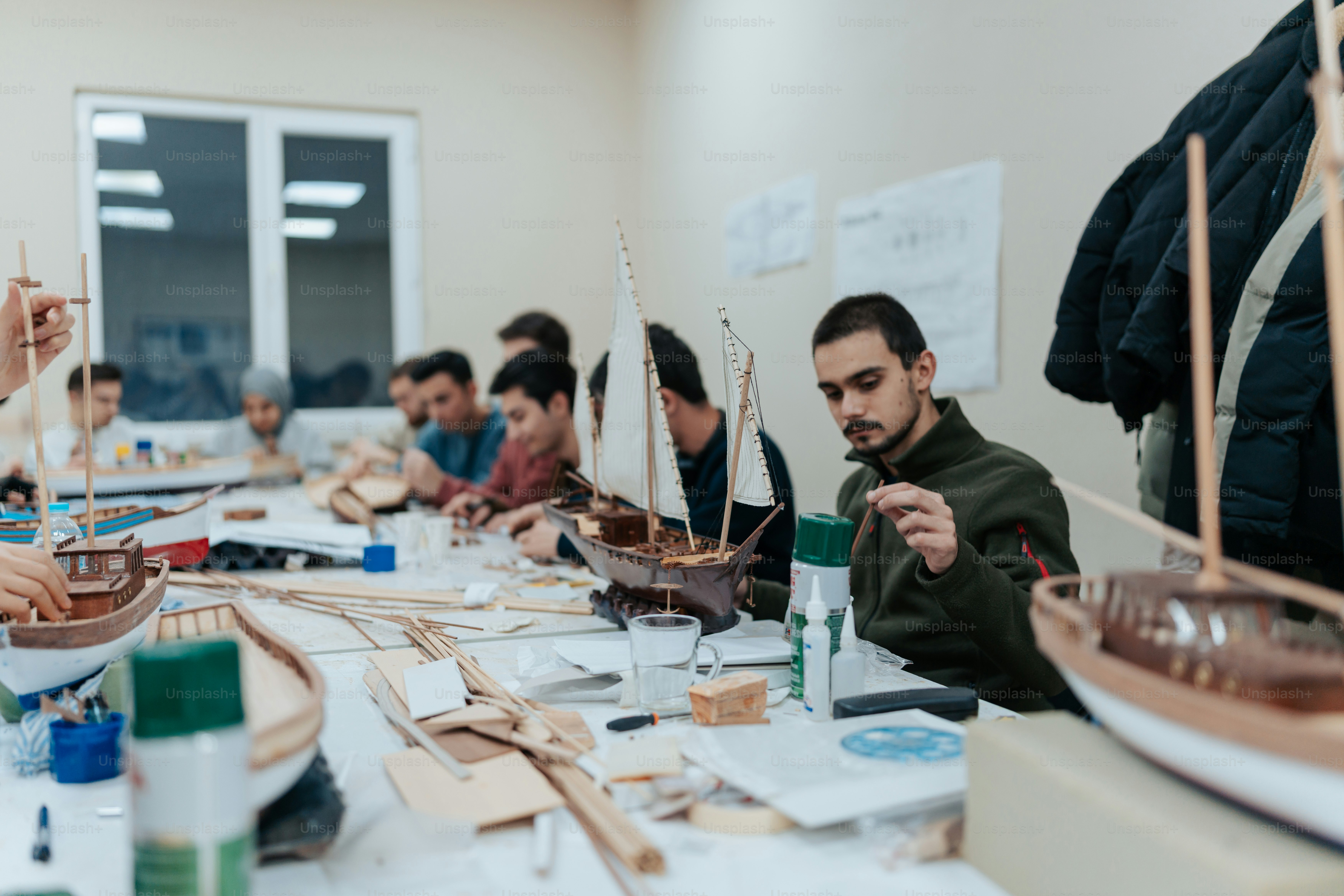 un groupe de personnes assises autour d’une table travaillant sur des bateaux en bois