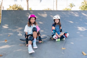 two young girls sitting on skateboards at a skate park