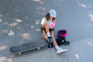 a young girl sitting on the ground next to a skateboard