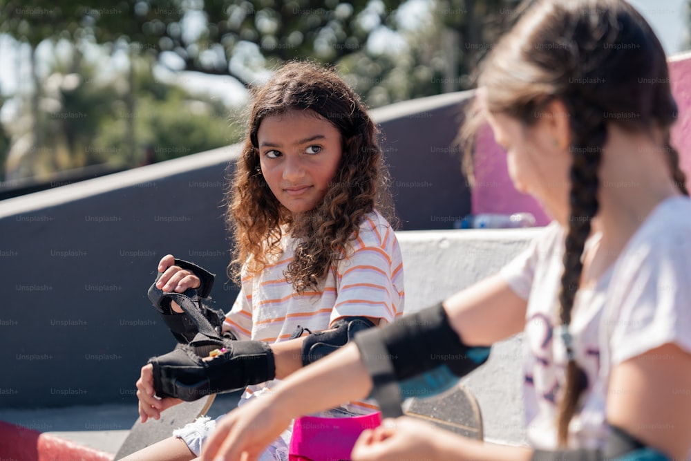 two young girls sitting on a skateboard at a skate park