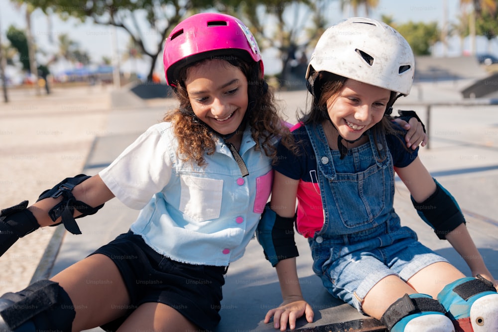 two young girls sitting on a skateboard at a skate park