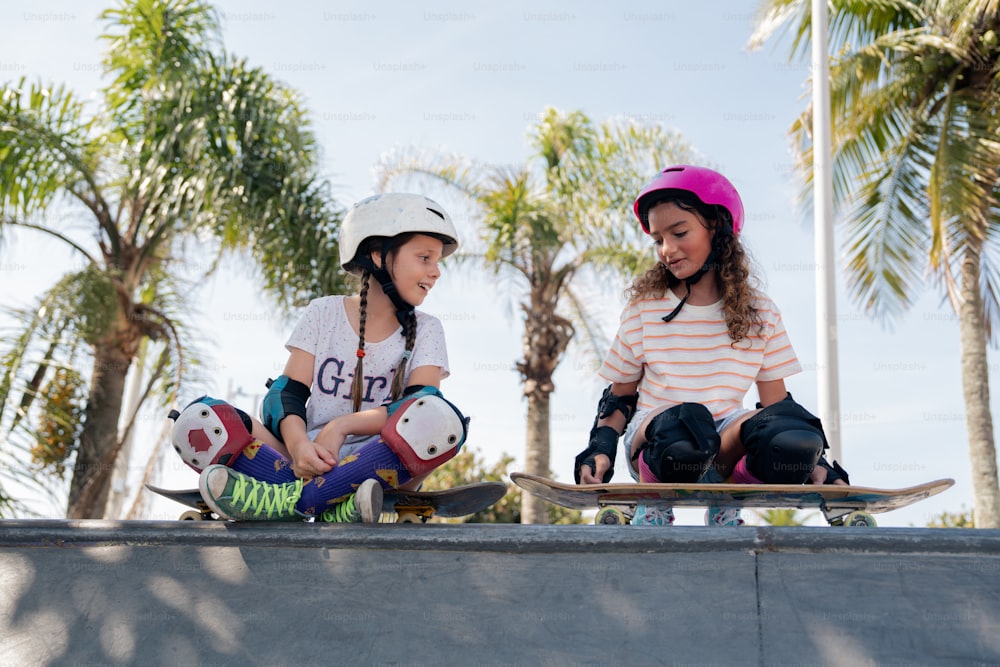 a couple of girls sitting on top of a skateboard ramp