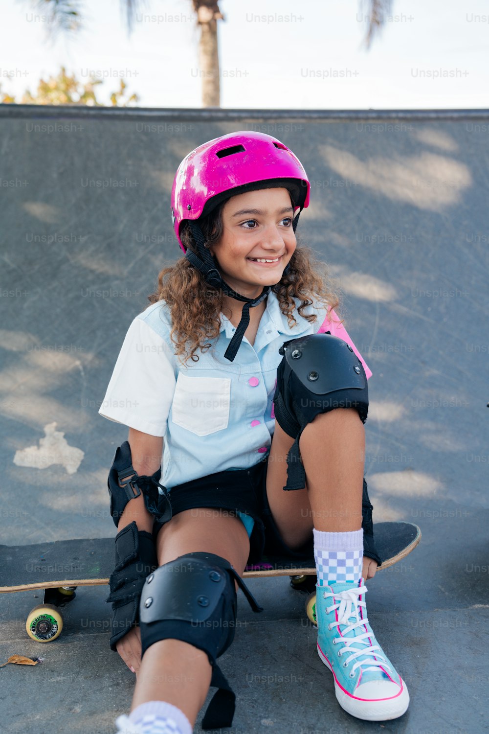 a young girl wearing a helmet and knee pads sitting on a skateboard