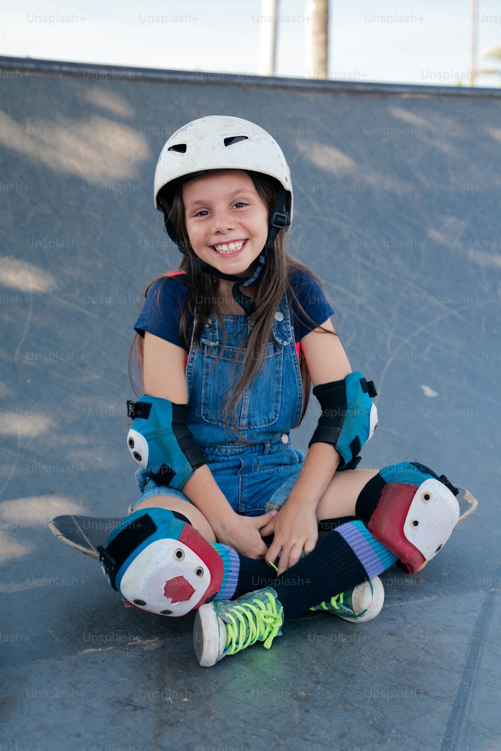 Ein junges Mädchen sitzt auf einem Skateboard in einem Skatepark