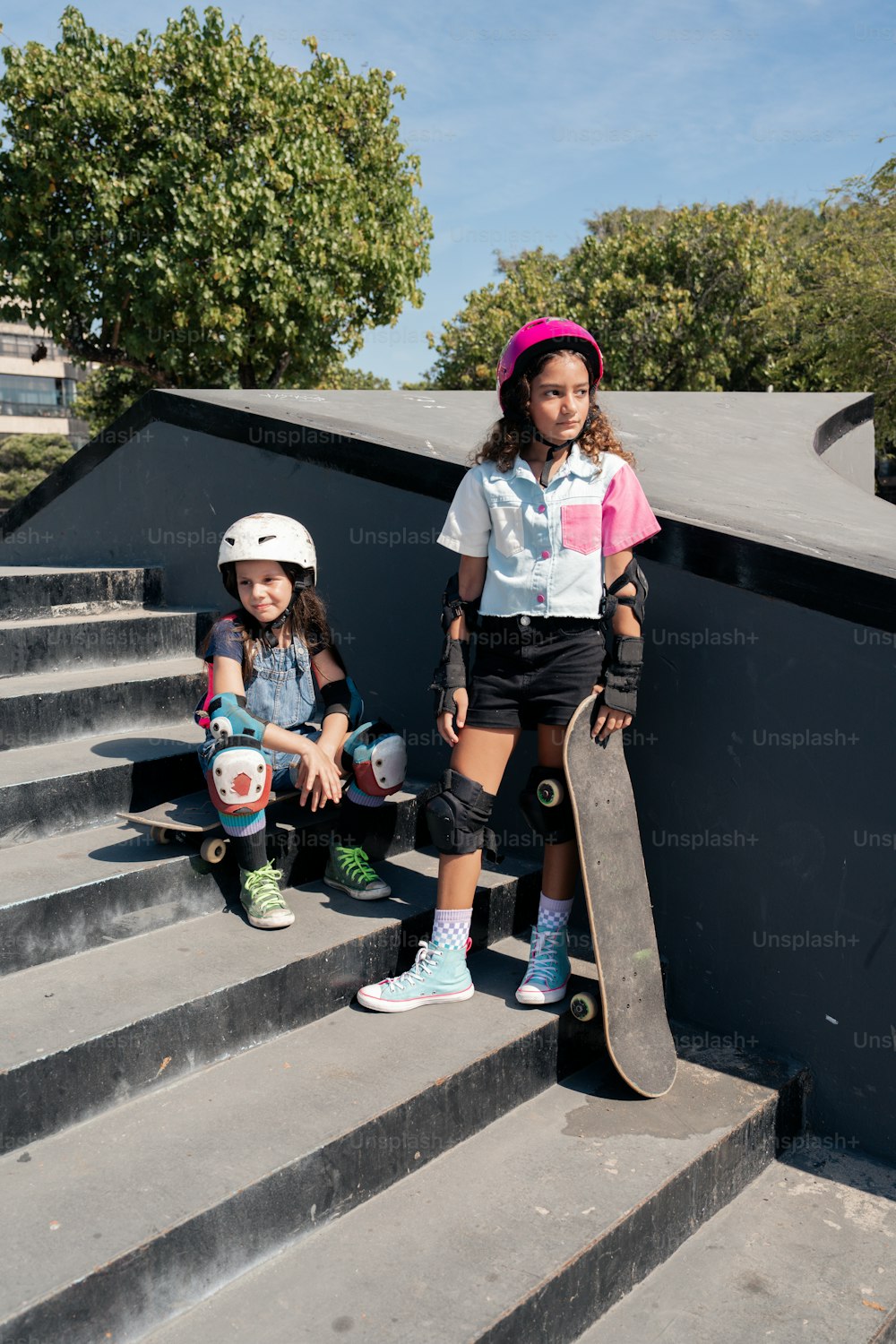 two young girls sitting on the steps with their skateboards