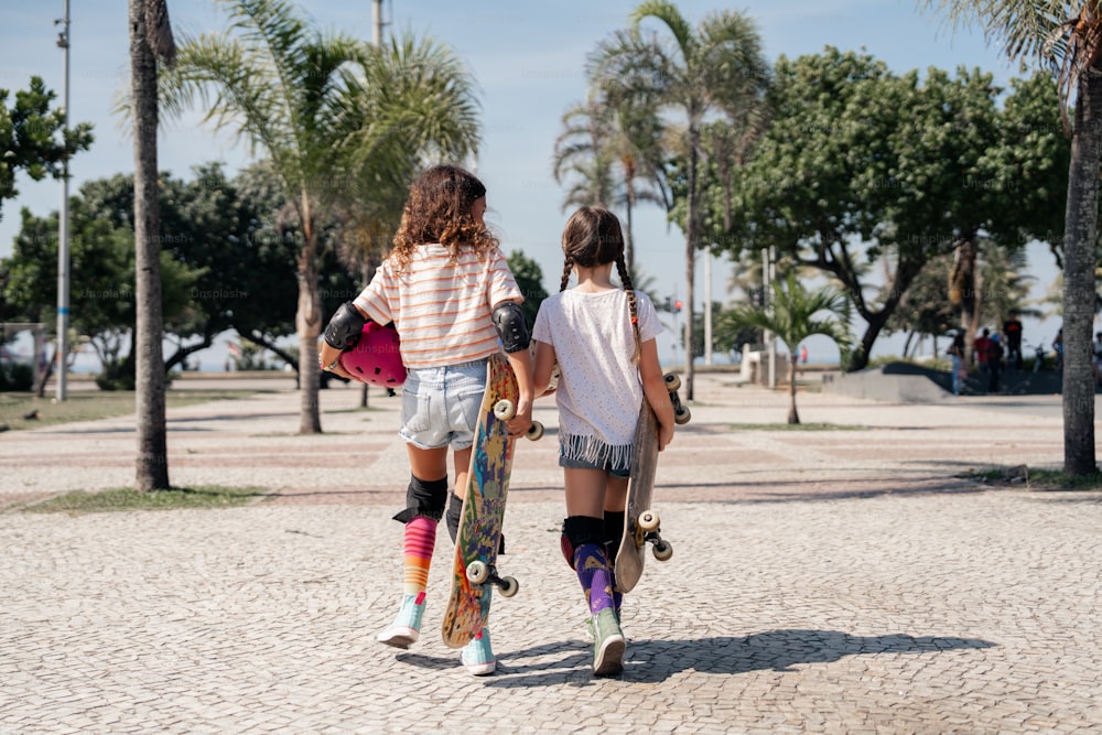 a couple of girls walking down a street with skateboards