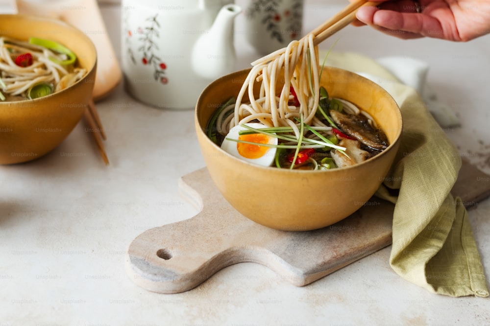 a person holding a wooden spoon over a bowl of noodles