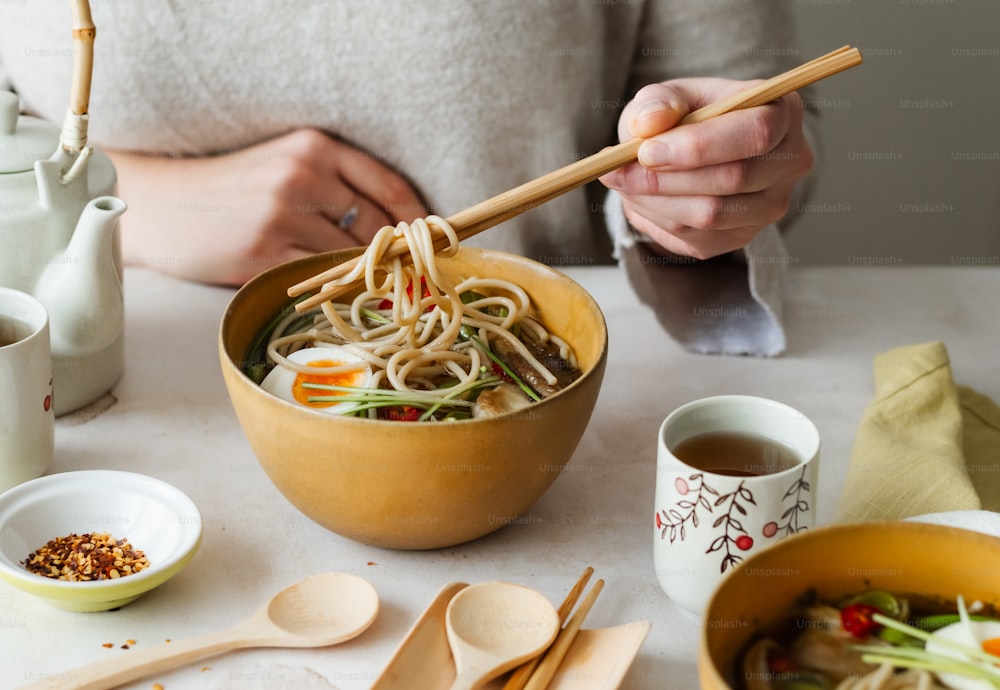 a person holding chopsticks over a bowl of noodles