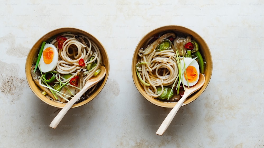 two bowls filled with noodles and vegetables on a table