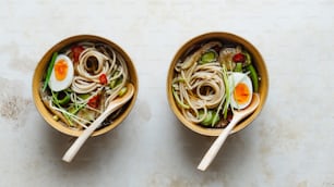 two bowls filled with noodles and vegetables on a table