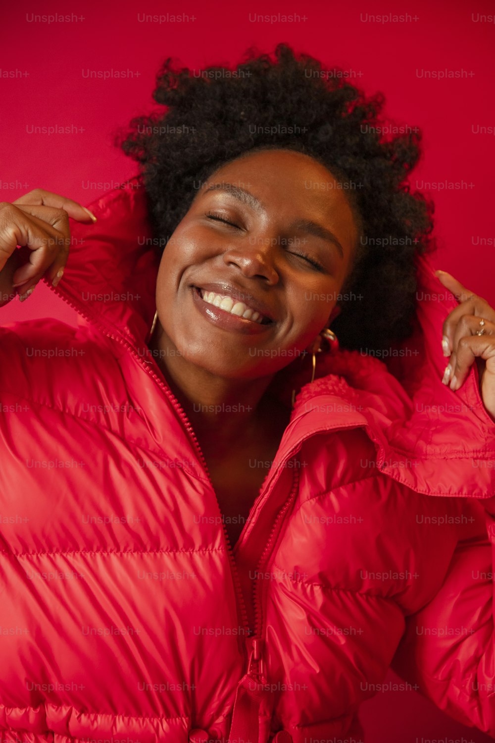 a woman in a red jacket smiling and holding her hands on her ears