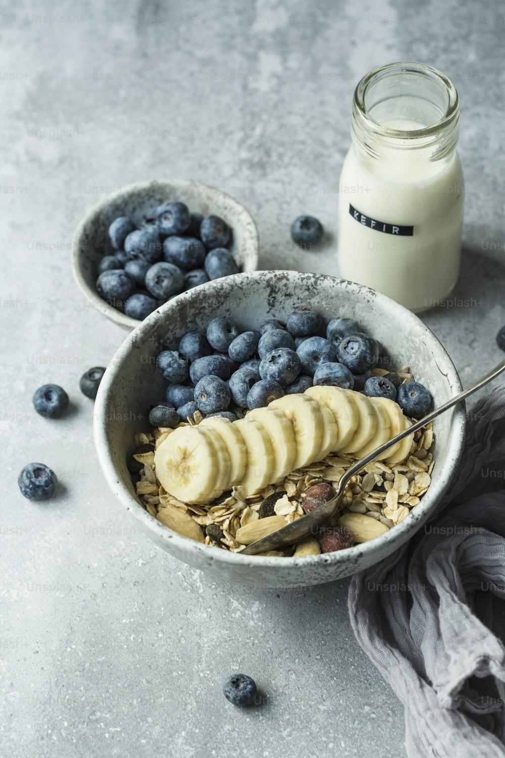 a bowl of cereal with bananas and blueberries next to a glass of milk
