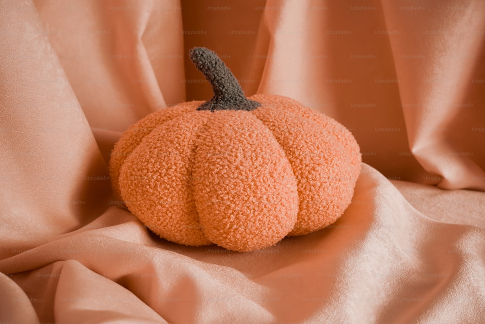 uma pequena abóbora laranja sentada em cima de uma cama