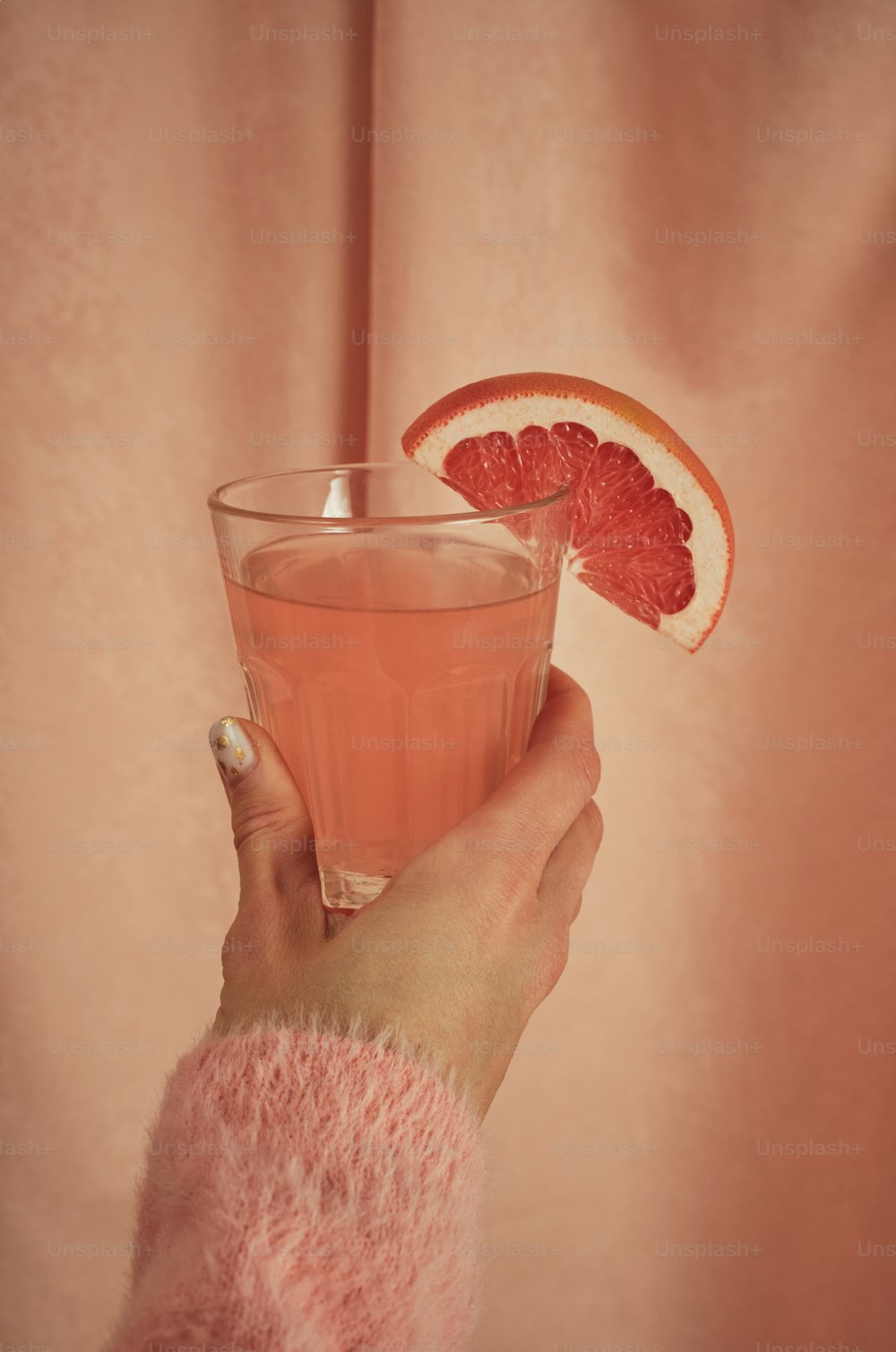 a person holding a glass with a grapefruit and a grapefruit slice