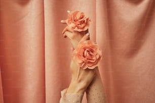 a woman's hands holding a flower in front of a pink curtain