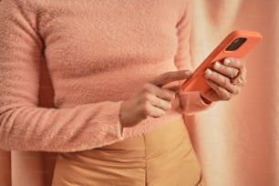 분홍색 스웨터를 입은 여성이 휴대전화를 들고 있다