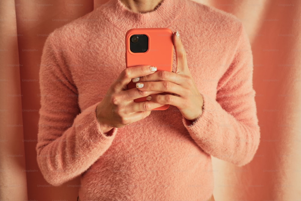 a woman in a pink sweater holding a cell phone