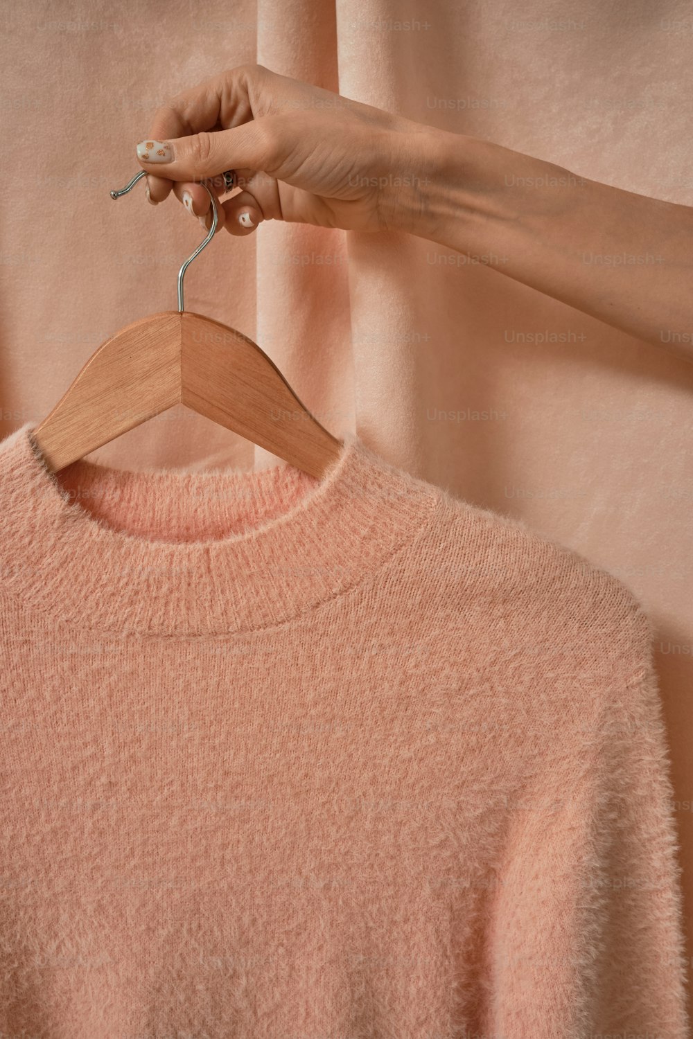 분홍색 스웨터 위에 나무 옷걸이를 들고 있는 여성의 손