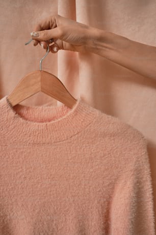 a woman's hand holding a wooden hanger over a pink sweater