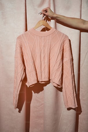 a pink sweater hanging on a wooden hanger