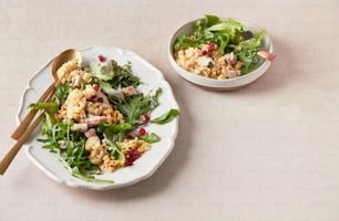 a white plate topped with a salad next to a bowl of salad