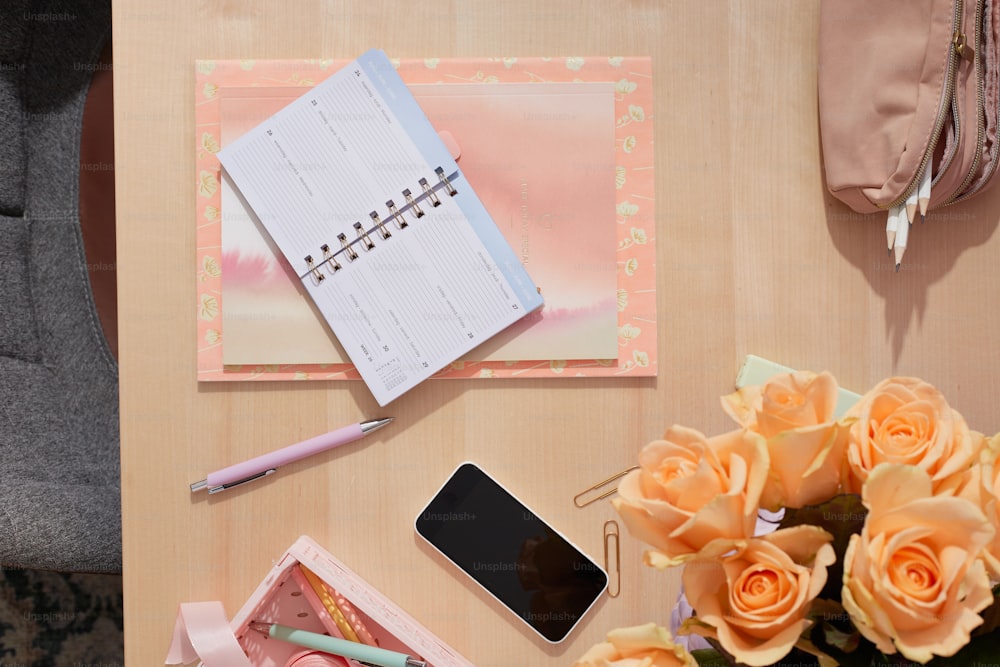 a desk with flowers, a cell phone and a notepad