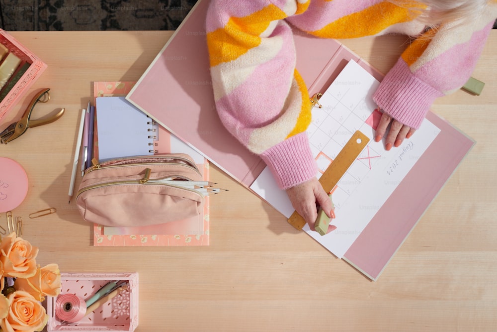 ピンクと黄色のセーターを着た女性がノートに書き物をしている