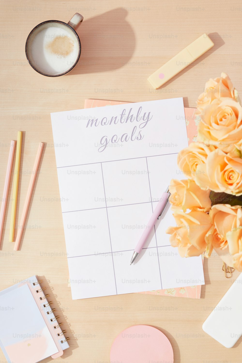 a desk with a notepad, pencils, flowers and a cup of coffee