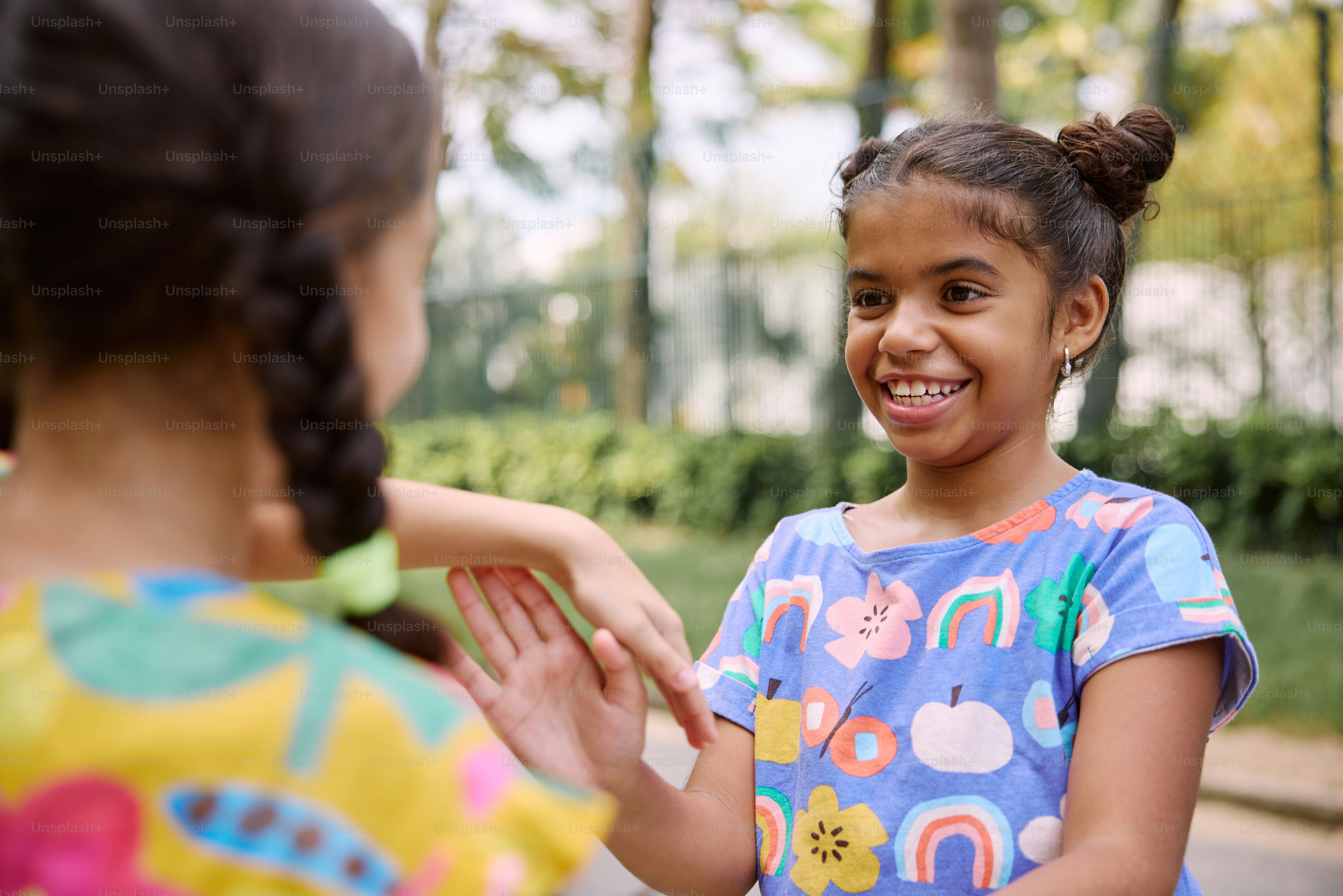 a young girl smiles as another girl holds her hand out to her