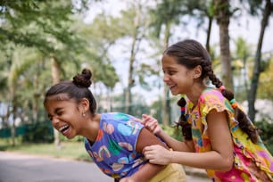 two young girls laugh as they ride a skateboard
