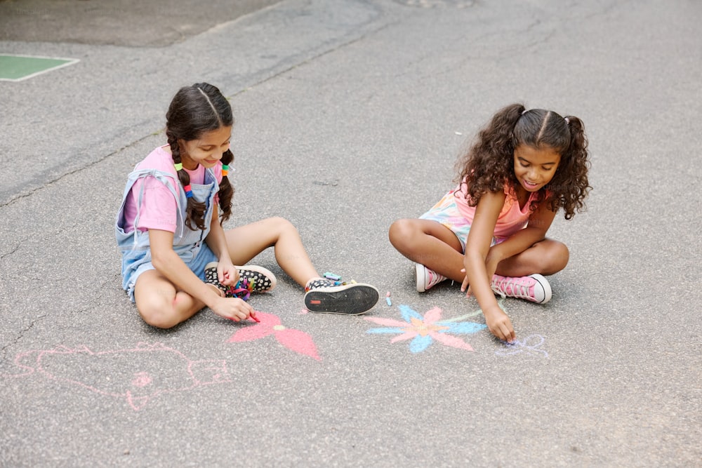 two girls sitting on the ground drawing with chalk