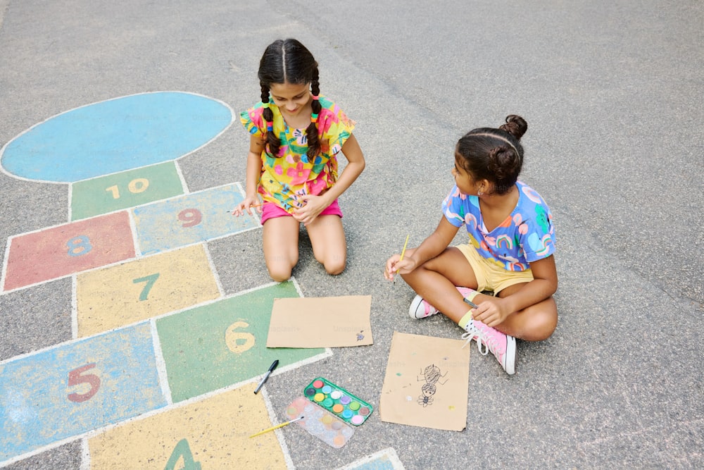 two young girls sitting on the ground drawing numbers