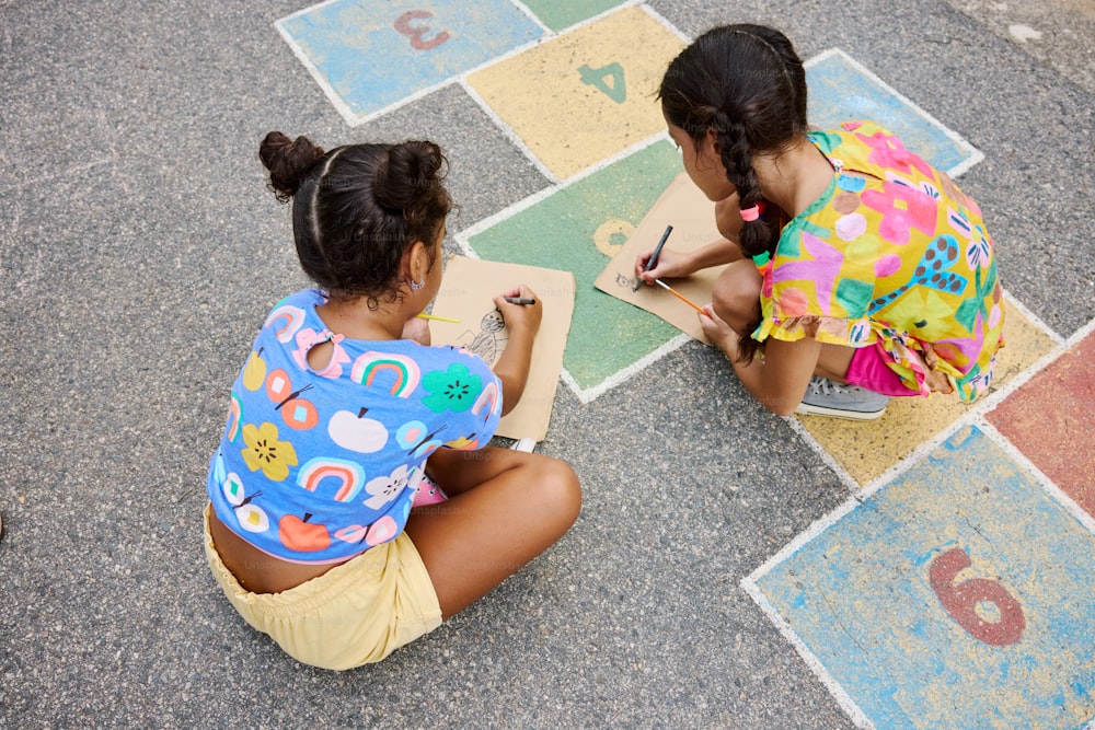 two young girls sitting on the ground writing numbers
