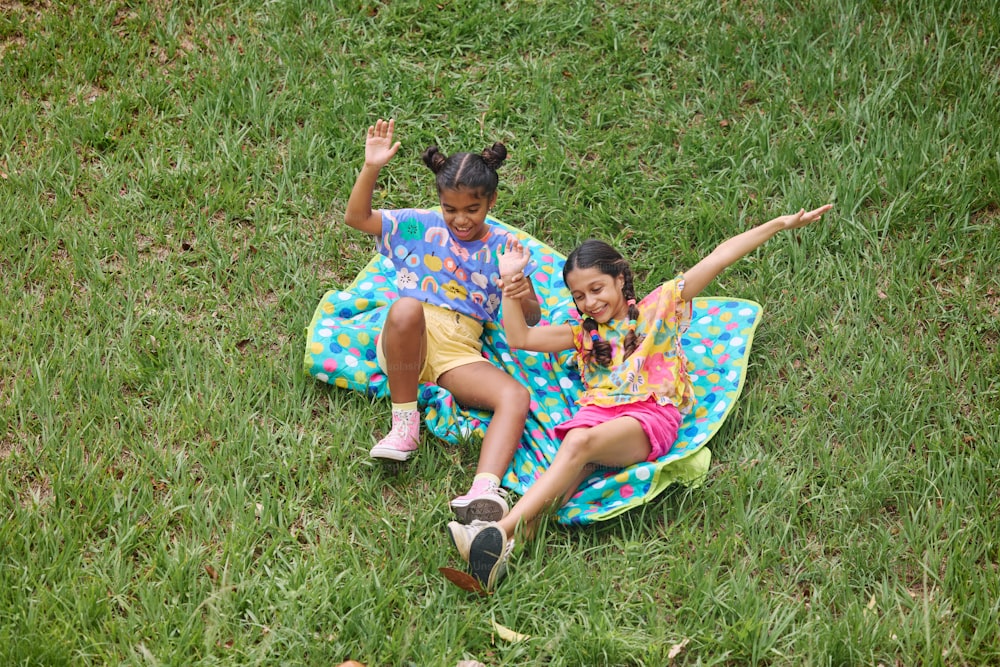 two girls sitting on a blanket in the grass