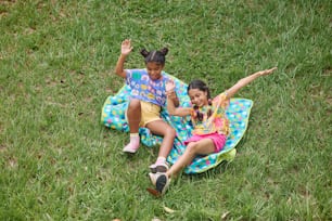 two girls sitting on a blanket in the grass