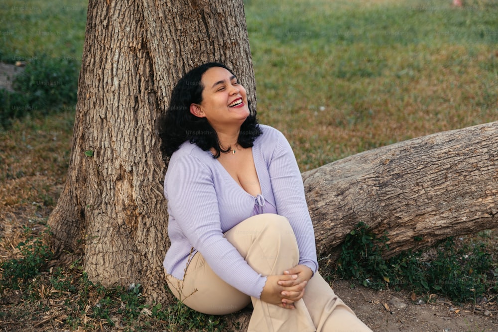 a woman sitting on the ground next to a tree