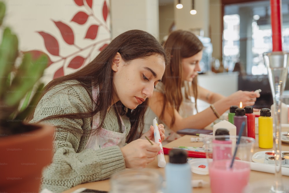 two girls are sitting at a table painting