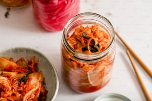 a glass jar filled with food next to a bowl of noodles