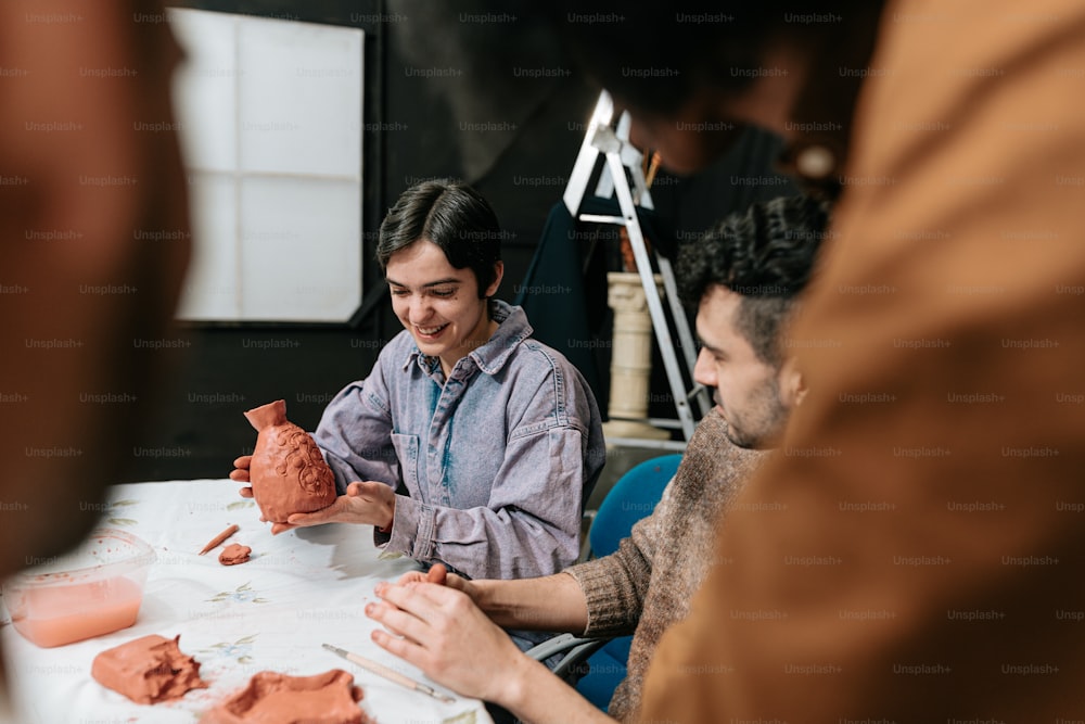 a group of people sitting around a table making clay