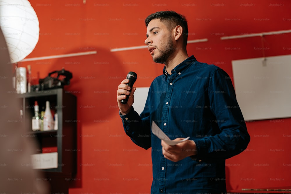 a man standing in front of a red wall holding a microphone