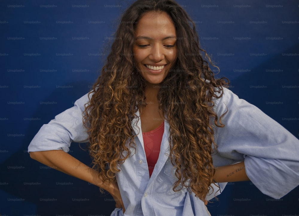 a woman with long curly hair smiling and holding her hands on her hips