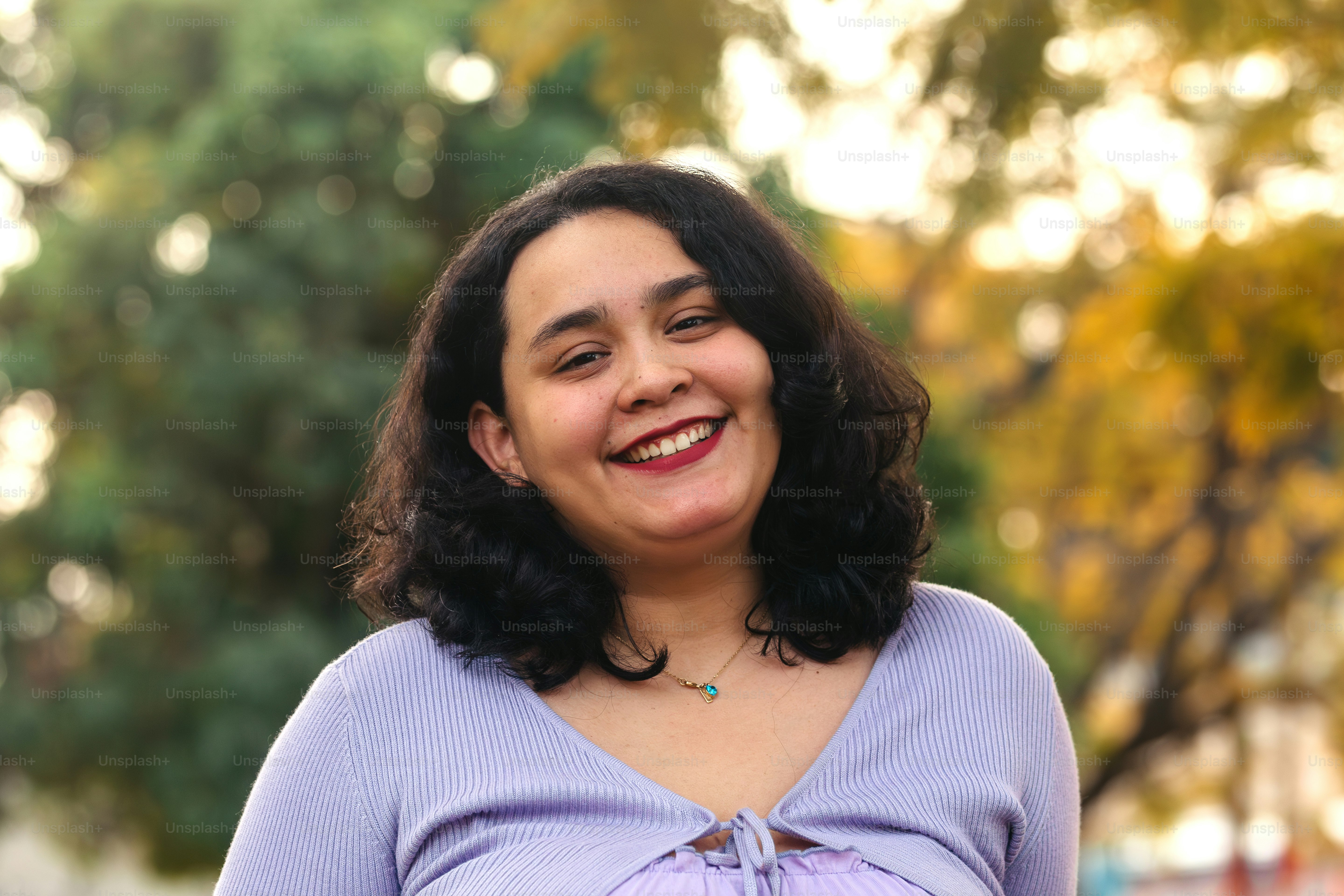 una donna sorridente in un top viola in piedi davanti agli alberi