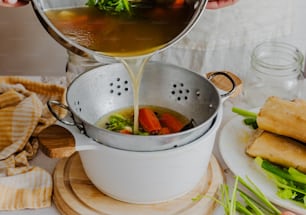 una persona vertiendo una olla de sopa en una olla