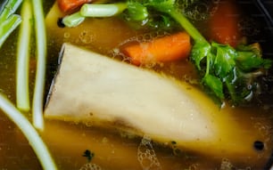 a bowl of soup with carrots, celery, and meat