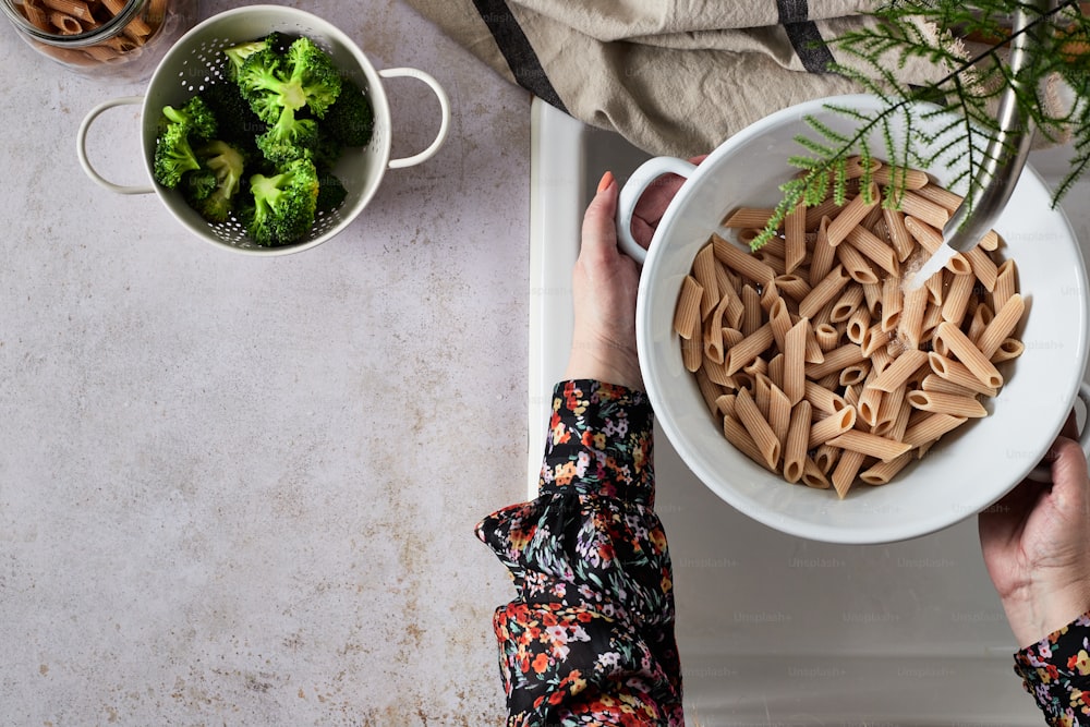 a person holding a bowl of pasta next to a bowl of broccoli