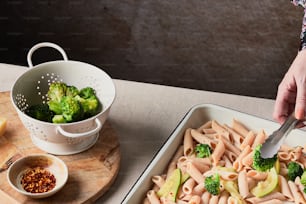 a person cutting broccoli on top of a pasta dish
